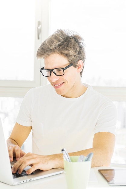 Hombre sonriente que lleva gafas usando la computadora portátil en casa