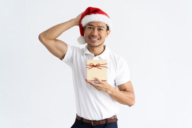 Hombre sonriente que lleva el sombrero de Papá Noel y que sostiene la caja de regalo