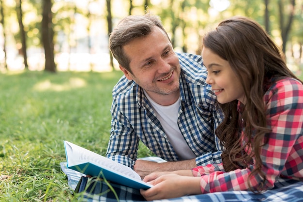 Hombre sonriente que mira su libro de lectura de la hija que miente en la manta