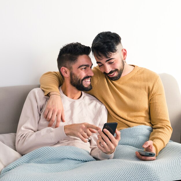 Hombre sonriente que muestra algo en el teléfono móvil a su novio