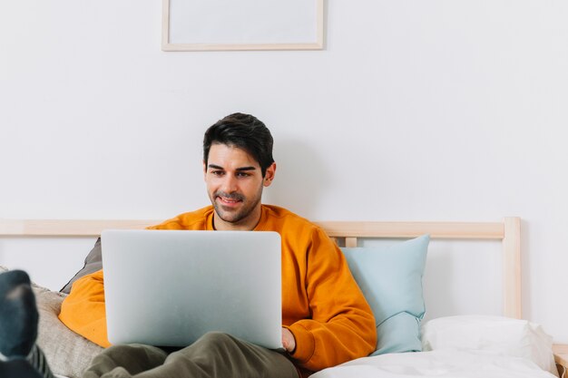 Hombre sonriente que navega la computadora portátil en la cama