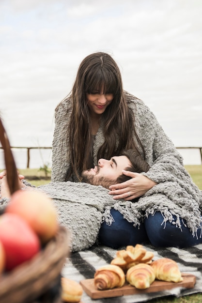 Hombre sonriente que se relaja en el regazo de su novia en la comida campestre