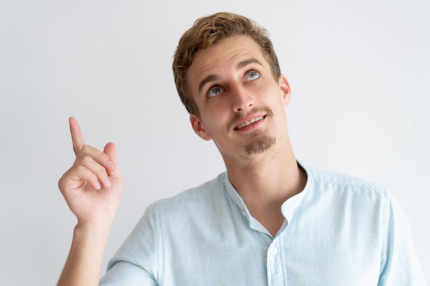 Hombre sonriente que señala el dedo y mirando hacia arriba