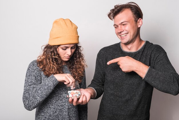 Hombre sonriente que señala el dedo a la mujer enferma que toma píldoras de la mano