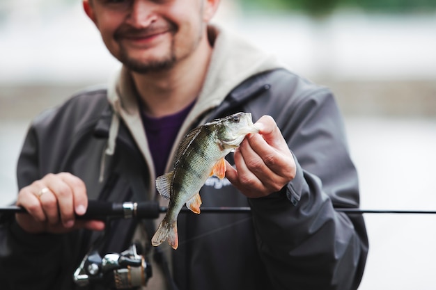 Hombre sonriente que sostiene la caña de pescar que muestra pescados cogidos