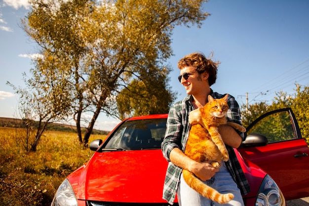 Foto gratuita hombre sonriente que sostiene un gato delante de un coche