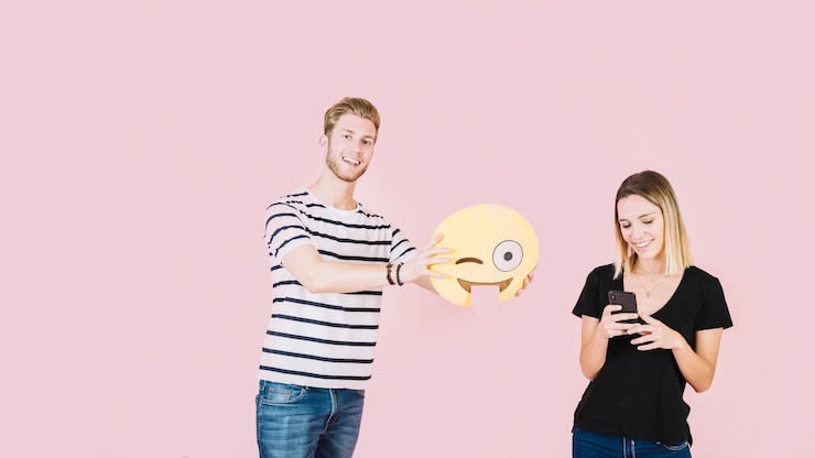 Foto gratuito hombre sonriente que sostiene el icono de emoji guiño cerca de mujer con teléfono móvil
