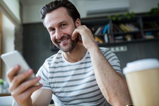 Hombre sonriente que sostiene su teléfono móvil en la tienda de café