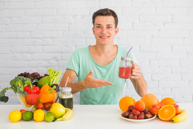 Hombre sonriente que sostiene el tarro de batido rojo que ofrece comida sana fresca