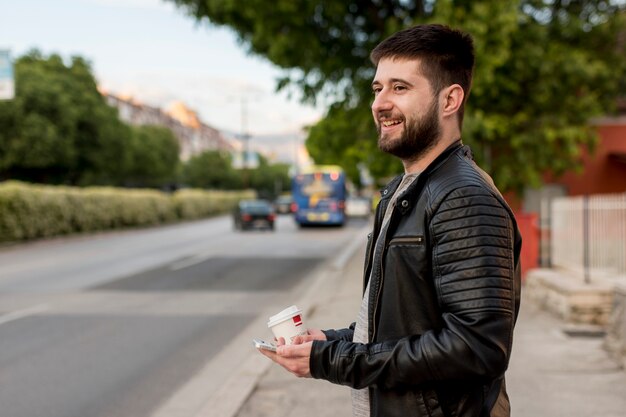 Hombre sonriente que sostiene la taza y el smartphone