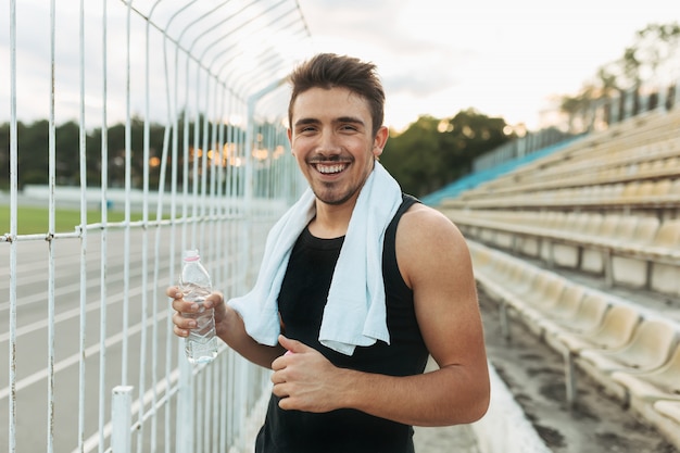 Foto gratuita hombre sonriente que sostiene la toalla blanca y la botella de agua.