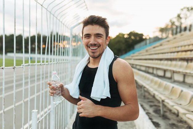 Hombre sonriente que sostiene la toalla blanca y la botella de agua.