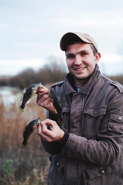 Hombre sonriente que sostiene tres pescados cogidos