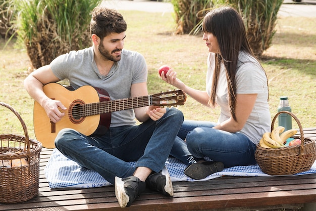 Foto gratuita hombre sonriente que toca la guitarra con su novia que sostiene la manzana roja disponible