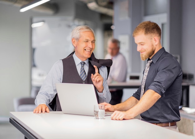 Hombre sonriente que usa la computadora portátil que se coloca con su encargado en el lugar de trabajo