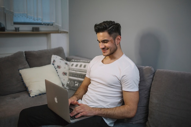 Hombre sonriente que usa la computadora portátil en el sofá
