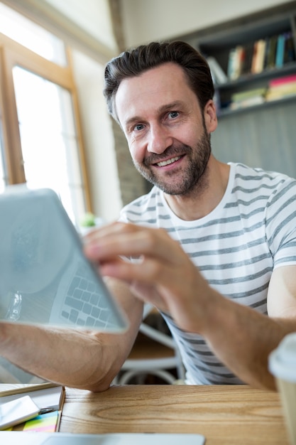 Hombre sonriente que usa la tableta digital en una cafetería