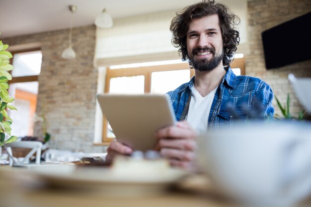 Hombre sonriente que usa la tableta digital en una cafetería