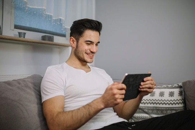 Hombre sonriente que usa la tableta en el sofá