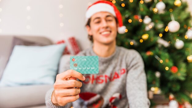 Hombre sonriente en Santa sombrero con tarjeta de crédito