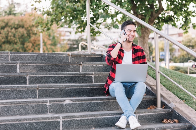 Hombre sonriente sentado en la escalera hablando por teléfono inteligente