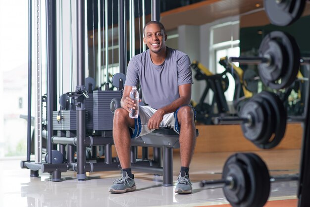 Hombre sonriente sentado en el gimnasio, sosteniendo una botella de agua