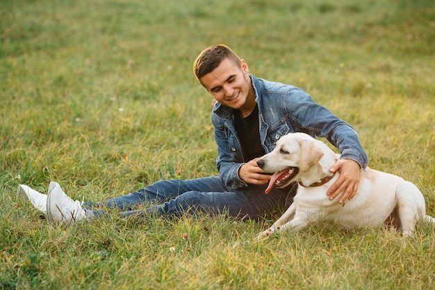 Hombre sonriente sentado en la hierba con su perro labrador en el parque