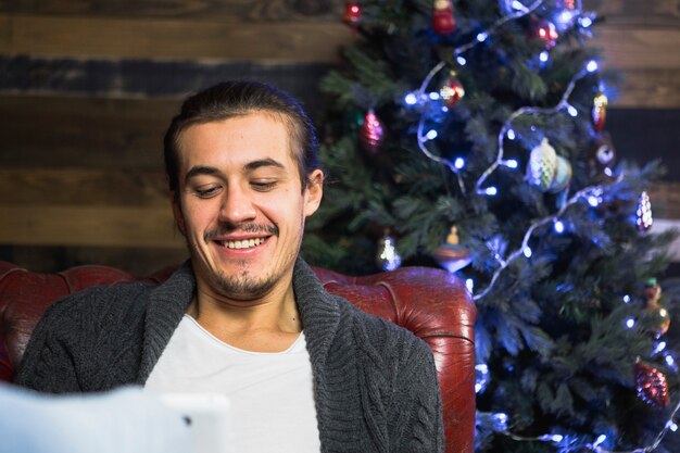 Hombre sonriente con smartphone en sofá en navidad