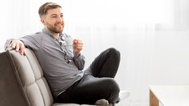 Hombre sonriente en el sofá tomando café
