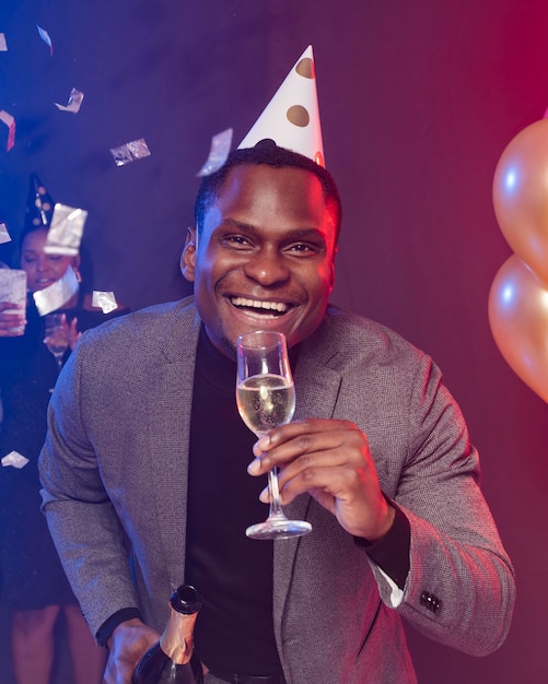 Hombre sonriente con sombrero de fiesta y sosteniendo un vaso