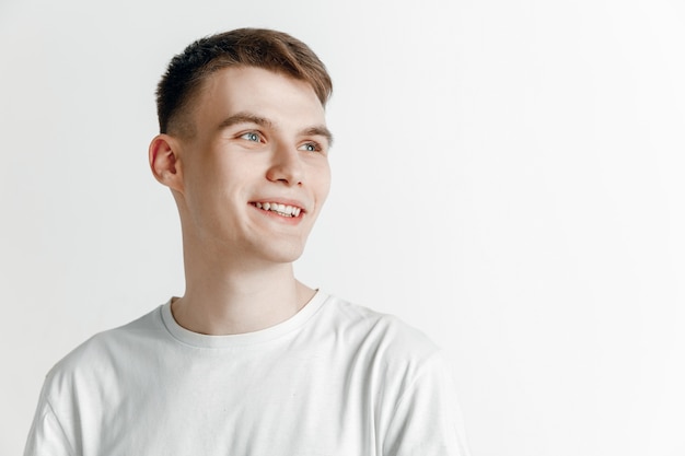 El hombre sonriente soñando joven está esperando chanses aislado sobre fondo gris. Soñador en estudio en camiseta blanca