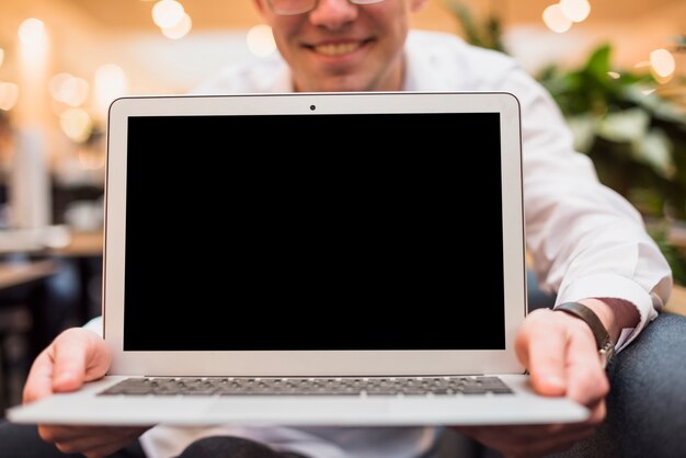 Hombre sonriente sosteniendo una laptop abierta con pantalla negra