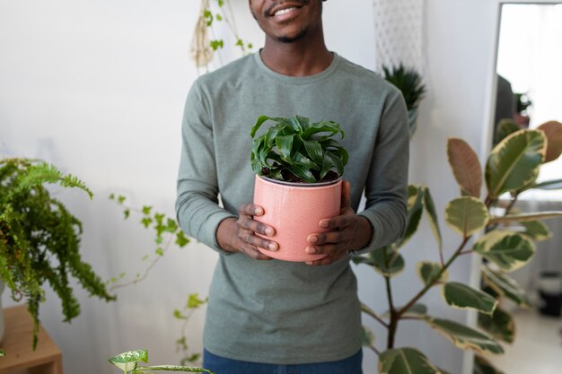 Hombre sonriente sosteniendo planta en casa vista frontal