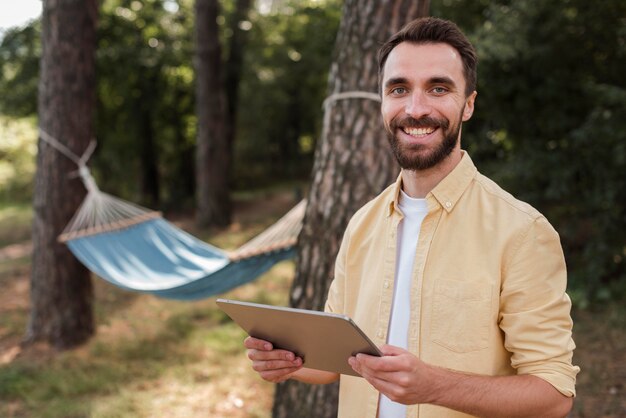 Hombre sonriente sosteniendo la tableta mientras acampa al aire libre