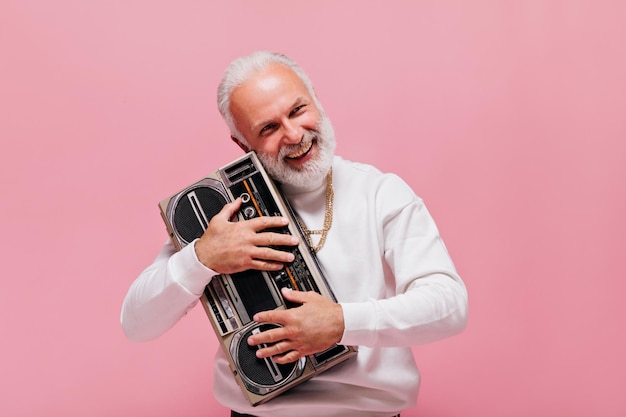 Foto gratuita hombre sonriente sosteniendo tocadiscos sobre fondo rosa chico adulto feliz con tatuajes y con cadenas de oro sonriendo sobre fondo aislado