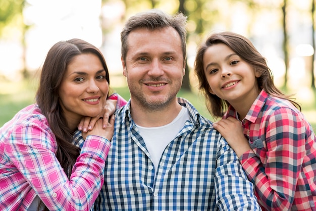 Hombre sonriente con su esposa e hija que miran la cámara en parque