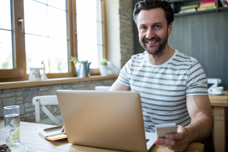 Foto gratuito hombre sonriente con su ordenador portátil y el teléfono móvil en la tienda de café