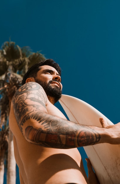 Hombre sonriente con tabla de surf contra el cielo azul