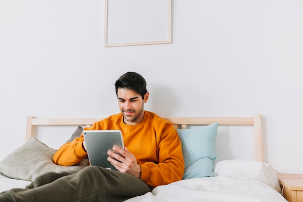 Hombre sonriente con tableta en la cama