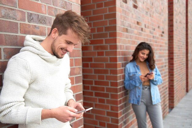 Hombre sonriente con teléfono inteligente y mujer en el fondo