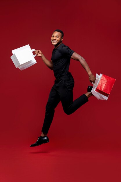 Hombre sonriente de tiro completo con bolsas de la compra.