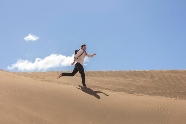 Hombre sonriente de tiro completo corriendo en el desierto