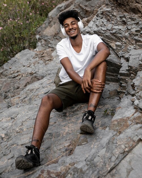 Hombre sonriente de tiro completo sentado sobre una roca