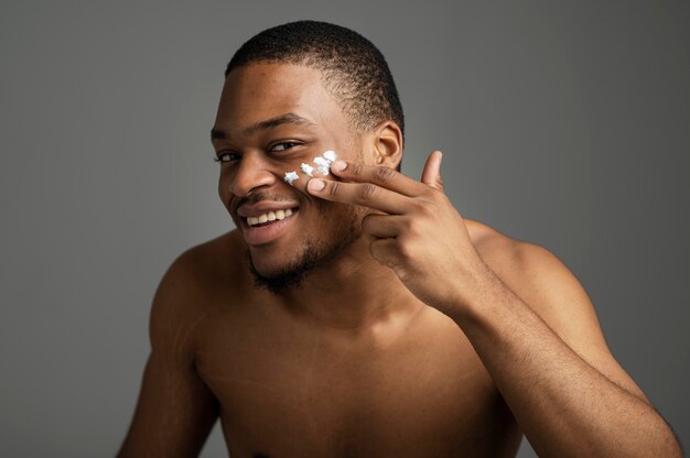 Hombre sonriente de tiro medio aplicando crema facial