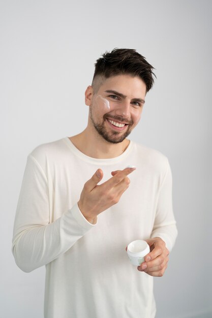 Hombre sonriente de tiro medio aplicando crema facial