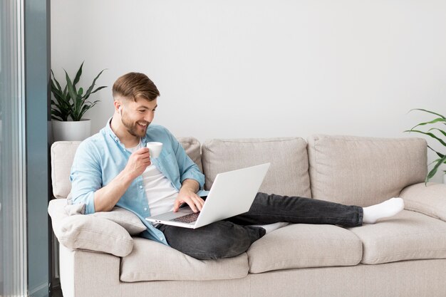 Hombre sonriente tomando café y usando laptop