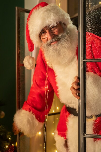 Hombre sonriente en traje de santa entrando a casa a través de la ventana