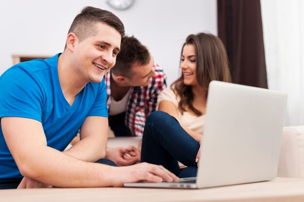 Hombre sonriente usando laptop con amigos en casa