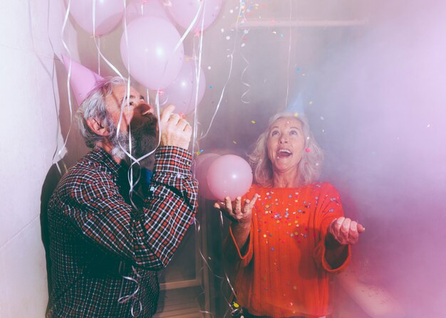 Hombre soplando el cuerno de fiesta y mujer lanzando el confeti al aire.