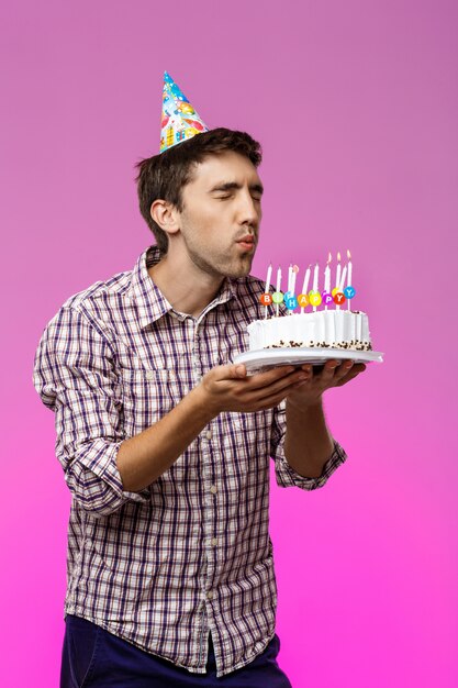 Hombre soplando velas en el pastel de cumpleaños sobre la pared púrpura.